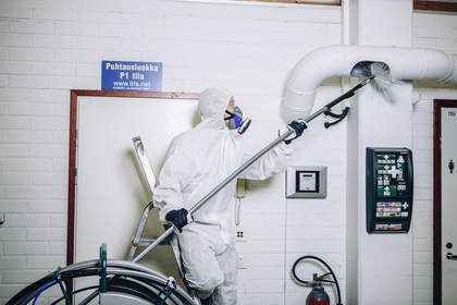 een man in een wit pak die een borstelmachine aanbrengt in een ventilatiekantaal