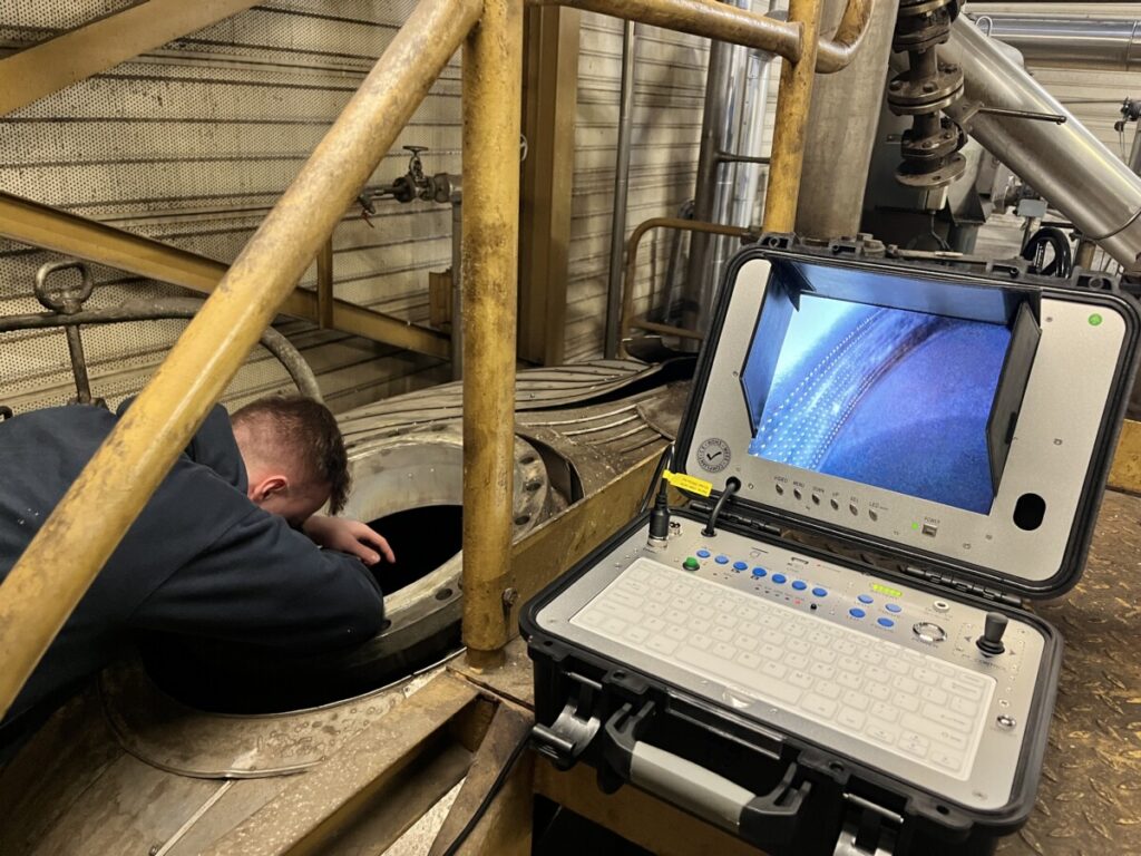 inspectiecamera in gebruik voor het inspecteren van een cycloon. een technicus kijkt in de opening van de cycloon, terwijl de inspectiecamera een beeld weergeeft op de monitor.
