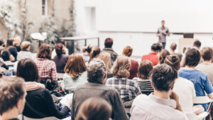 de aula in een universiteit waar de studenten luisteren naar de docent die vooraan staat en spreekt.