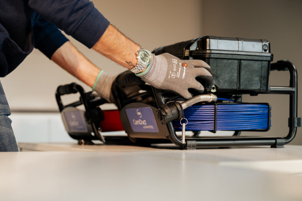 een man met werkhandschoenen die voor een tafel staat waarop een inspectiecamera ligt en die vastneemt.