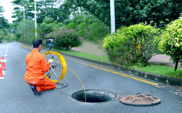 een ontstopper aan de slag met inspectiecamera met open dekspel van rioolput.